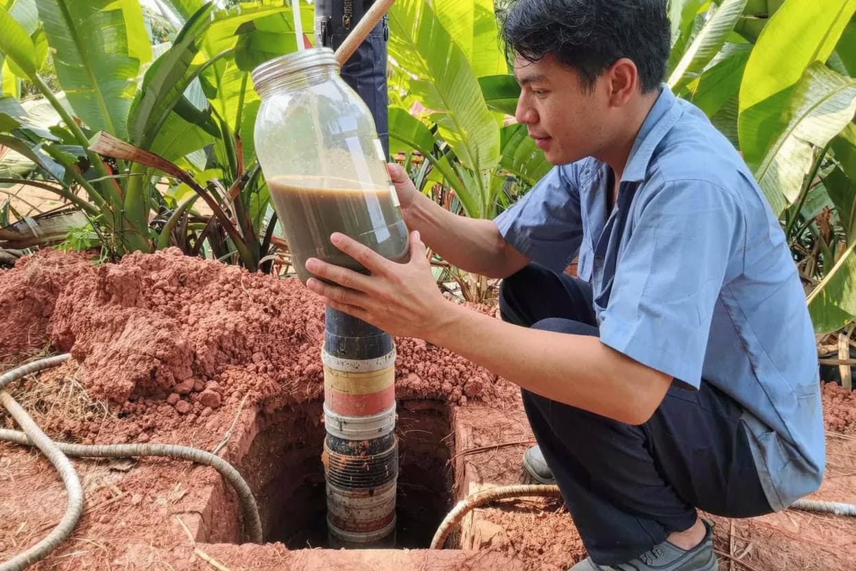 ช่างถือโหลน้ำบาดาลขุ่นที่มีตะกอน ข้างปากบ่อบาดาลที่เปิดอยู่บนเกาะสมุย